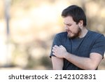 Small photo of Stressed man scratching itchy arm complaining in nature