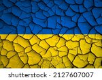 Small photo of Ukraine national blue and yellow flag on a mud texture of dry cracks on the ground