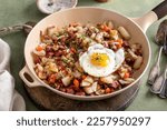 Small photo of Corned beef hash with potatoes, cabbage and carrot in a cast iron pan topped with a fried egg