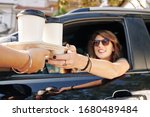 Waiter giving disposable tray with two cups of take out coffee to pretty smiling female driver