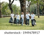 Group of cheerful young volunteers carrying bags of trash they picked on campus or in city park