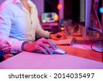 Close-up image of entrepreneur using computer mouse when working at office desk at night, pink light