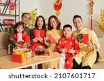 Small photo of Smiling family members in ao dai dresses holding red lucky money envelopes
