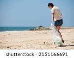 Small photo of Young woman walking on beach with big plastic bag and collecting trash brought by sea wave