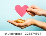 Hand showing red heart paper shape and coins on blue background. Love and money concept.