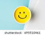 Yellow smiley face or happy emotion at work, on paper cup and papers over blue background. Happy work day concept.