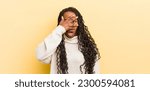 Small photo of black pretty woman looking shocked, scared or terrified, covering face with hand and peeking between fingers