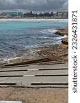 Small photo of Cleated concrete boat ramp descending from Ben Buckler Point to Flat Rock sandstone area at the northeasternmost end of North Bondi Beach, visible in the background. Sydney-New South Wales-Australia.