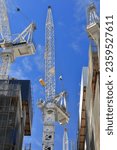 Small photo of Tower cranes on top of buildings under construction on Collins Street south side featuring slewing units-operating cabins-luffing jibs-lifting hooks, slightly cloudy blue sky. Melbourne-VIC-Australia.