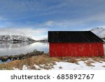 Rolling steel boathouse-red wall-black roof. Gimsoystraumen flow-Olderfjorden mouth. Mts.Kleppstadheia-Kvasstinden-Botntinden-Rismalstindan-Smatindan-Varden on back. Lyngvaer-Austvagoya-Lofoten-Norway