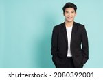 Smiling young Asian businessman in black suit isolated on green background