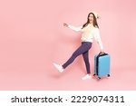 Small photo of Happy Asian woman traveler walking and holding luggage isolated on pink background, Tourist girl having cheerful holiday trip concept, Full body composition
