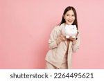 Small photo of Happy Asian woman holding white piggy bank isolated on pink background, Saving money and financial economize concept