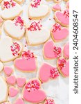 Small photo of Decorating heart-shaped sugar cookies with pink and white royal icing for Valentine's Day.