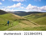 Small photo of A female hiker and their dog descending from Windy Gyle towards Trows in the Cheviot Hills, Northumberland, England, UK.