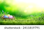Small photo of Three painted easter eggs in a birds nest celebrating a Happy Easter on a spring day with a green grass meadow and blurred grass foreground and bright sunlight background with copy space.