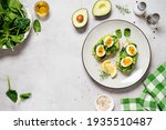 Healthy toast with sliced avocado, boiled eggs, spices and fresh spinach. Delicious breakfast or snack on gray stone background. top view, space for text