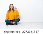 Small photo of Young caucasian woman sitting on the floor isolated on white background intending to realizes the solution while lifting a finger up