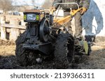 Small photo of Man farmer working in field ploughing the land with a plough on a farm. Ploughman on a walk behind motor cultivator. Season processing soil in village. Organic cultivate natural products. Agriculture