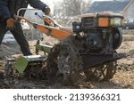 Small photo of Man farmer working in field ploughing the land with a plough on a farm. Ploughman on a walk behind motor cultivator. Season processing soil in village. Organic cultivate natural products. Agriculture