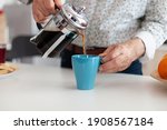 Close up of senior man pouring hot coffee from french press in kitchen during breakfast. Elderly person in the morning enjoying fresh brown cafe espresso cup caffeine from vintage mug, filter relax