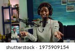 Small photo of Focused shot on smartphone recording african blogger woman talking looking at camera during online podcast. Content creator streaming online broadcast, blogger discussing wearing headphones.