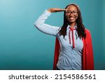 Patriotic justice defender saluting with respect while standing on blue background while smiling at camera. Brave and proud happy superhero woman wearing mighty hero cloak while making soldier salute.