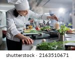 Small photo of Culinary expert putting fresh chopped herbs in pan while cooking gourmet dish for dinner service at fine dining restaurant. Head chef preparing organic meal in professional kitchen.