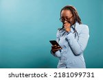 Small photo of Upset young woman crying after reading tragic news on smartphone device while standing on blue background. Sad unhappy adult person in tears while reading unfortunate message.