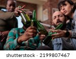 Multiethnic group of friends saying cheers and clinking beer bottles to celebrate party event, feeling happy about reunion. People toasting with alcohol drinks at hangout, leisure activity. Close up.