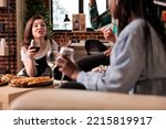 Small photo of Exalted woman shouting, talking loudly arguing to different ethnicities people group at friends living room apartment dinner, drinking wine, eating bread sticks, cheese.