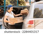 Woman delivering pizza to office by car side view, young fast food restaurant courier holding boxes pile. Pizzeria delivery service caucasian employee in headphones carrying lunch