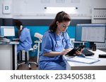 Small photo of Young nurse checking appointments list on digital tablet in busy medical office. Adult woman healthcare specialist working with technology at hospital desk with stethoscope around neck
