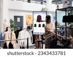 Client using touch screen board in trendy clothing store, shopping for fashion collection items in shop. Young buyer buying clothes on interactive monitor, self ordering concept.