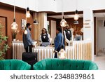 Small photo of Young African American couple standing at hotel front desk with luggage, paying for room with credit card while checking out. Friendly smiling female receptionist serving tourists checking guests in