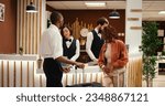 Small photo of Husband and wife on honeymoon trip requesting special room amenities from asian receptionist in hotel lobby. Helpful concierge personnel presenting holiday package deal to couple in luxury resort
