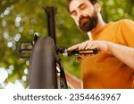 Small photo of Fit and active male cyclist fastening bike pedal safely for outside cycling. Dedicated sporty man performing bike maintenance skillfully repairing bicycle crank arm with essential work tool.
