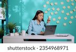 Small photo of Bored employee working dull monotonous lacklustre tedious office job. Asian businesswoman playing with pen while working on laptop in dreary uninspiring workplace over blue studio background