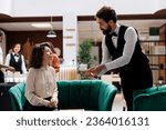 Small photo of Bellboy giving coffee cup to manager, providing excellent concierge service to supervisor sitting in lounge area at reception. Hotel employee talking to administrator, serving beverage.
