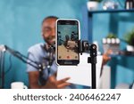 Small photo of Blogger making giveaway while live streaming on smartphone screen closeup. Web content creator announcing contest and showing prize gift using mobile phone on tripod for video recording