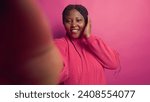 Small photo of African american female vlogger talking on online video call with webcam, grasping smartphone. Enthusiastic black woman doing vlog content with digital mobile phone against vibrant pink background.