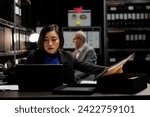 Small photo of Asian private investigator starting criminal investigation case, comparing criminal investigation details. Detective woman in archive file cabinet office filled with criminology folders