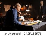 Small photo of Elderly suitmaker overthinking comissioned business suit required by customer. Old experienced couturier working on sartorial bespoken clothing designs in tailoring studio workspace