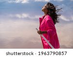 Small photo of sensitive dreaming mixed race woman in pink clothes with closed eyes, meditation, enjoying moment nature. hair romantically wiggle wind. mindfulness of life representation. Blue sky with clouds