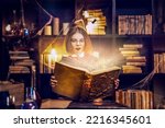 Small photo of Surprised caucasian little girl in witch Cosplay reads magic book while holding magic wand, Halloween costume. Halloween party.