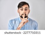 Portrait of young caucasian man covering his mouth with finger isolated on white background. Asks for silence, keep secret, shh gesture