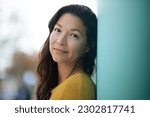 Close-up portrait of pretty young asian woman leaning to a wall outside and staring at camera