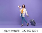 Small photo of Beautiful young Asian tourist woman walking with trolley suitcase, passport and air ticket about to fly, studio shot purple color isolated background