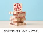 Small photo of Target symbol on collapsing wooden blocks with words distraction, incompetence, procrastination, fear, envy, self-doubt. Concept of importance of identifying challenges that hinder progress towards a