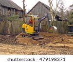 Small photo of NICA, LATVIA - MARCH 21, 2009: Young man worker with yellow mini excavator is building grovel road in country farm yard.
